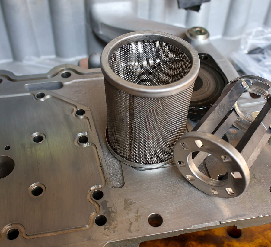 Metal in-tank suction strainer installed in hydraulic pump assembly, showing fine mesh screening and threaded connection